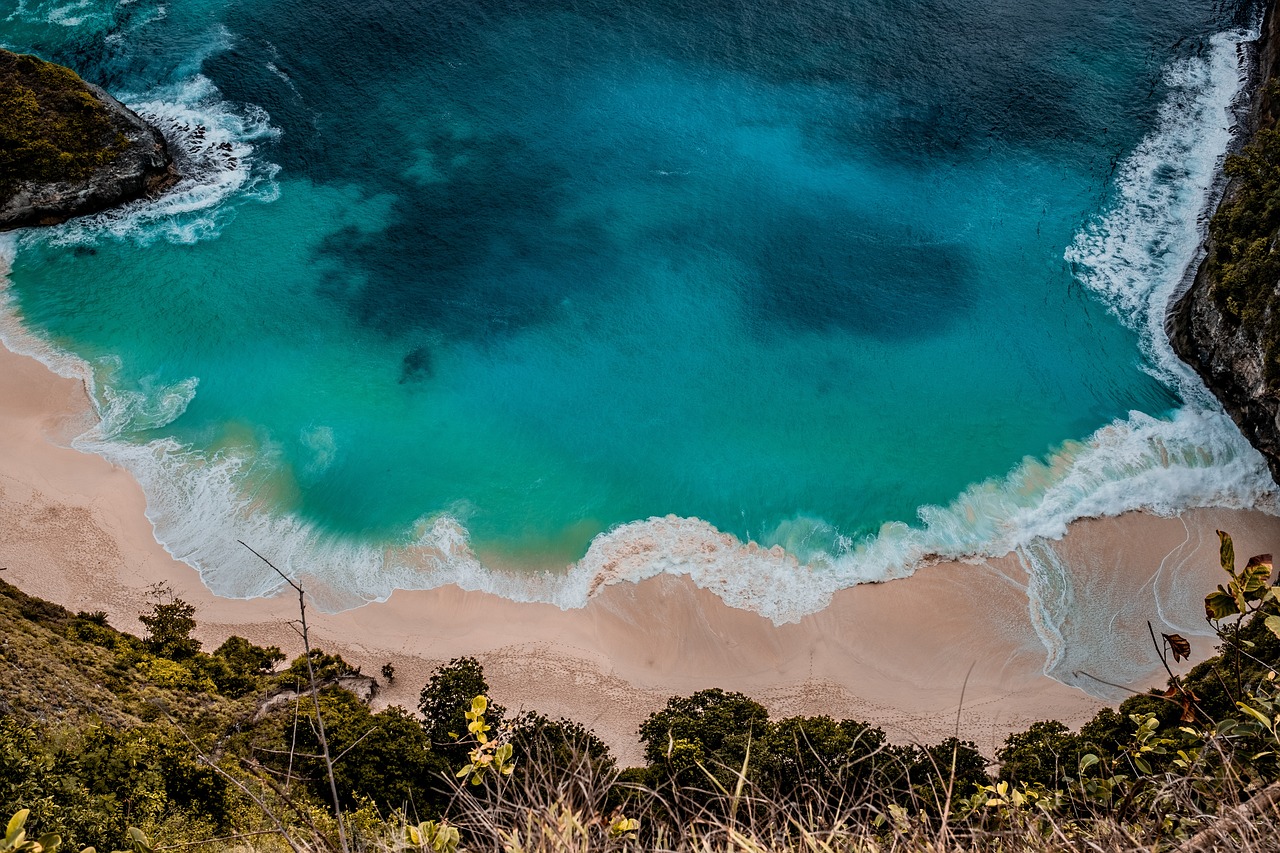 An aerial view of waves meeting a sandy beach between green headlands