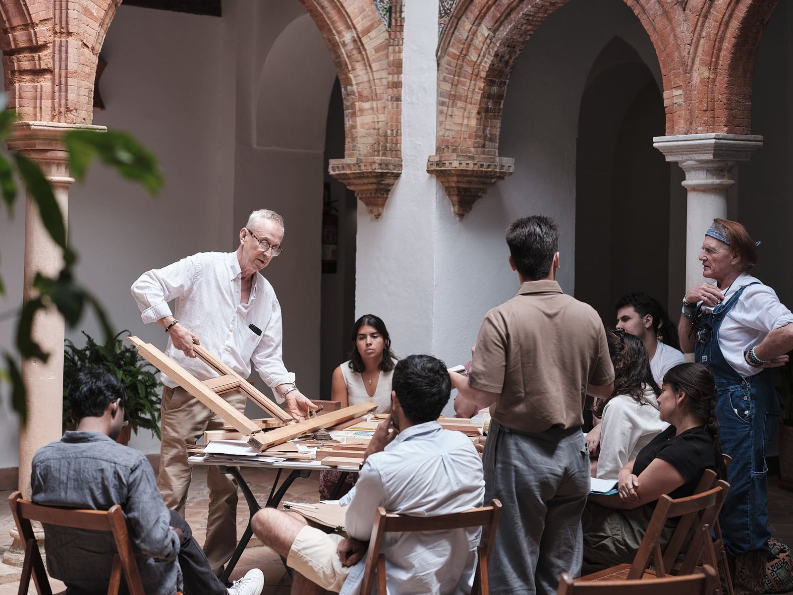 A tutor showing wooden building models to a group of participants in a brick arched courtyard