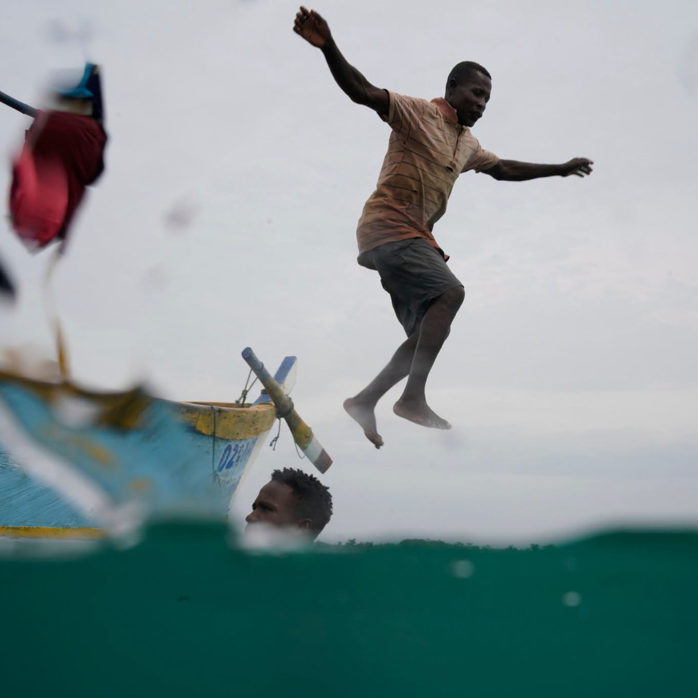 Fisherman captured mid-jump beside a small boat, half above and half below the waterline, on the Save Our Seas Foundation grant page